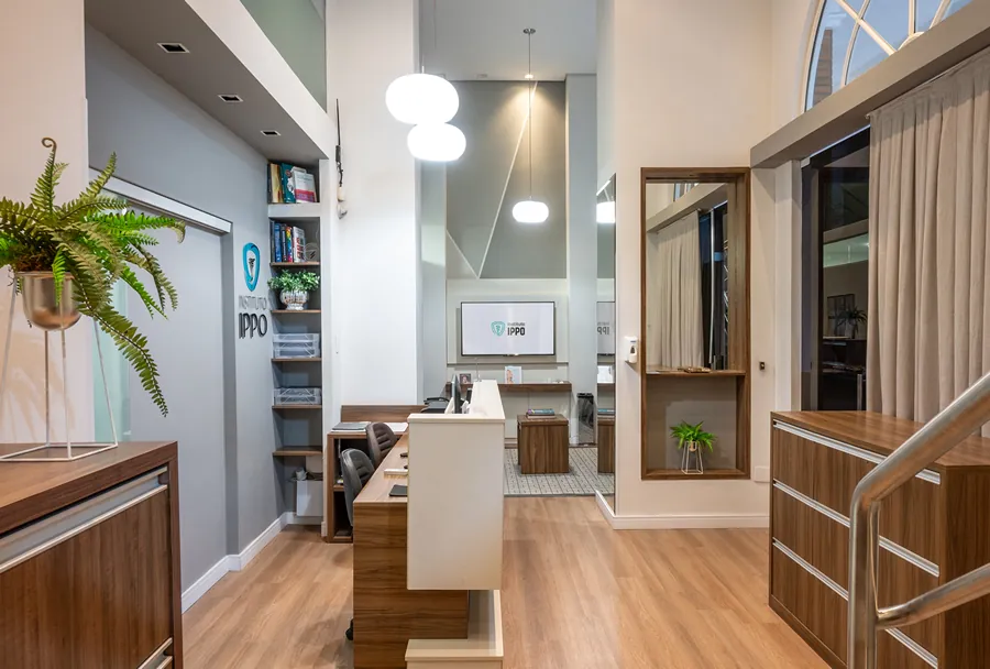 Recepção do Instituto IPPO com uma decoração moderna, incluindo uma mesa de atendimento, plantas e uma parede com o logotipo da instituição.