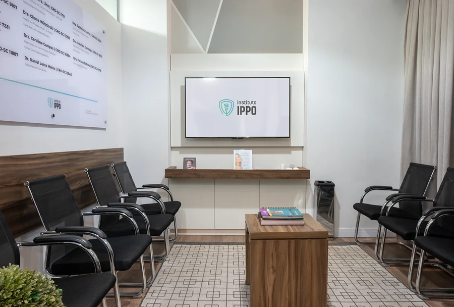 Sala de espera do Instituto IPPO com cadeiras alinhadas, uma televisão com o logotipo da instituição e uma decoração moderna e acolhedora.